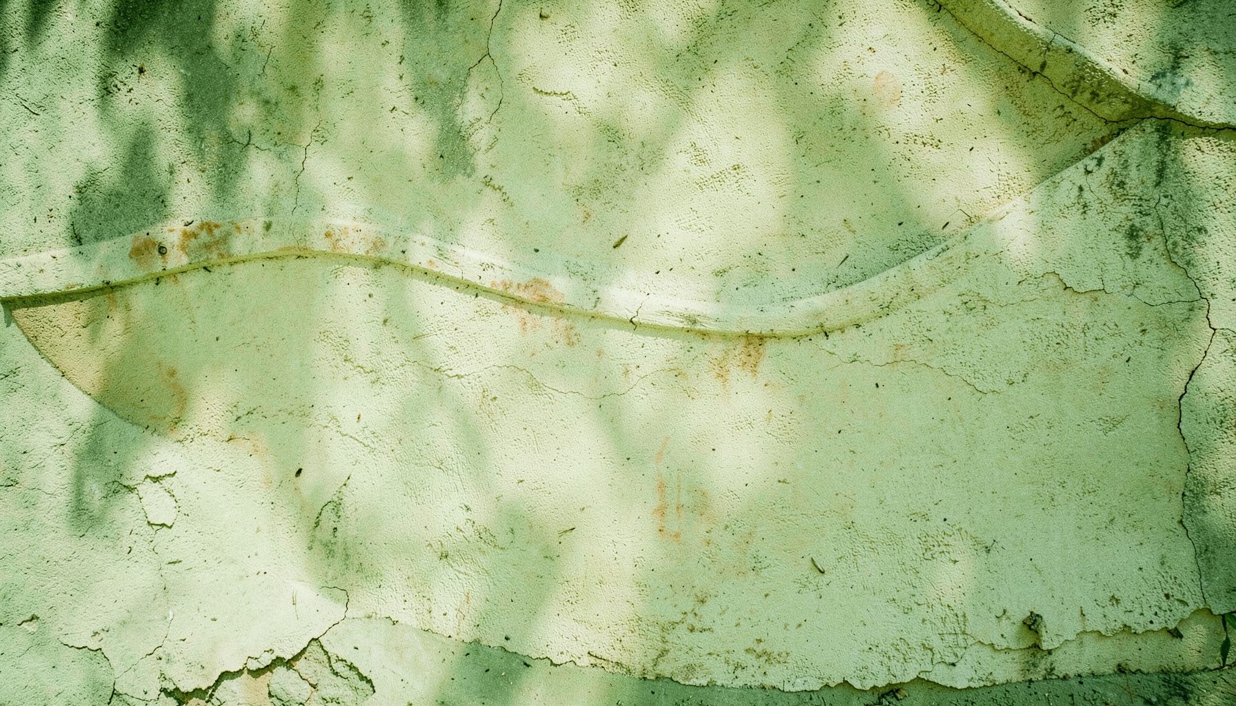 A weathered stucco wall with a boat-shaped contour curving gracefully, painted in soft cream with faint traces of aged pigment, dappled by afternoon light.